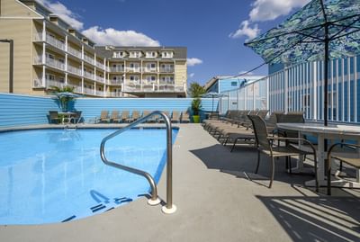 Pool area surrounded by blue walls and lounge chairs, with a clear sky and fluffy clouds above at Madison Beach Motel