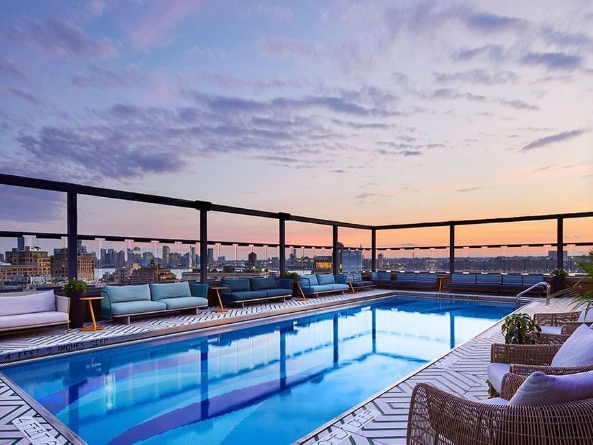 Gansevoort Rooftop pool with lounge chairs and a view of the sunset and Manhattan skyline.