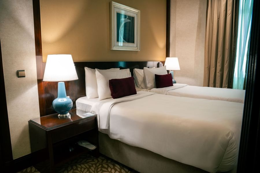 Modern guest twin bedroom featuring wall art with burgundy pillows and blue bedside lamps at Saja by Warwick Makkah