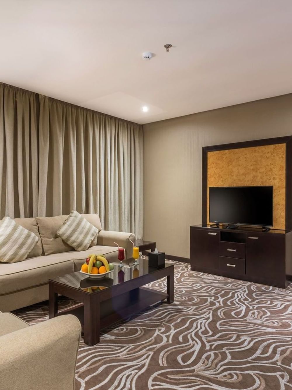 Junior Suite features Beige sofas by a coffee table with fruit under long curtains at Naviti by Warwick Al Khobar