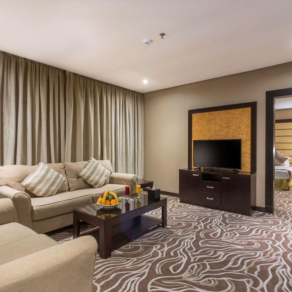 Junior Suite features Beige sofas by a coffee table with fruit under long curtains at Naviti by Warwick Al Khobar