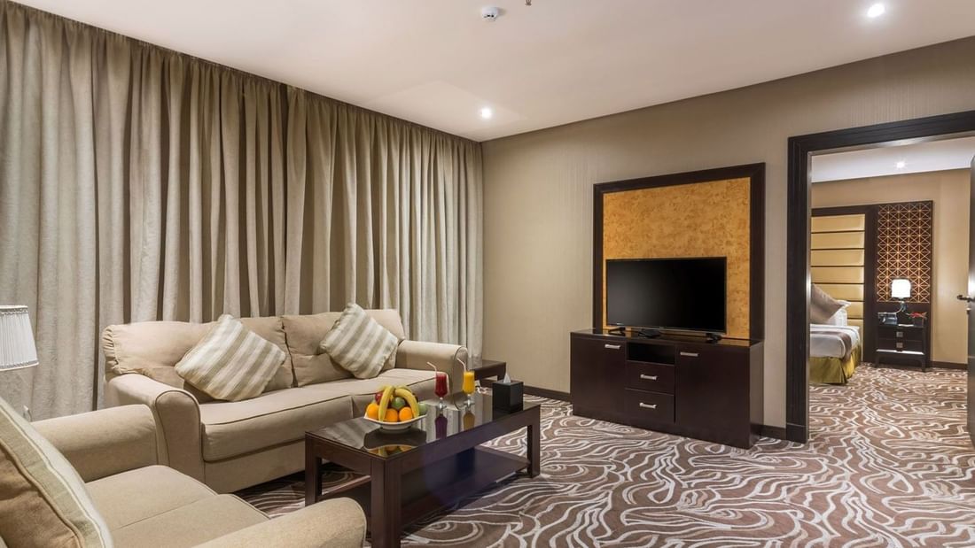 Junior Suite features Beige sofas by a coffee table with fruit under long curtains at Naviti by Warwick Al Khobar