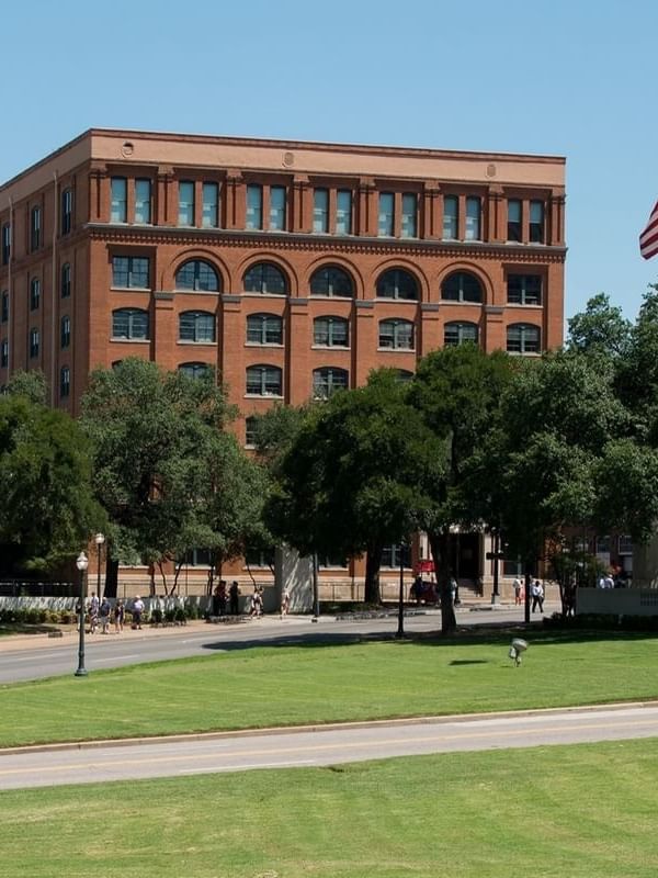 The historic red-brick building of the Sixth Floor Museum surrounded by trees near Warwick Melrose Dallas