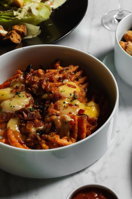 Bowl of crispy waffle fries topped with melted cheese, crispy bacon, and fresh herbs at Cypress & Oak Steakhouse, Frankfort
