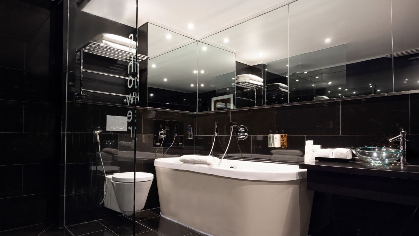 Sleek bathroom in The Saffron Suite at The May Fair Hotel London, featuring a bathtub, glass sink, and large mirror