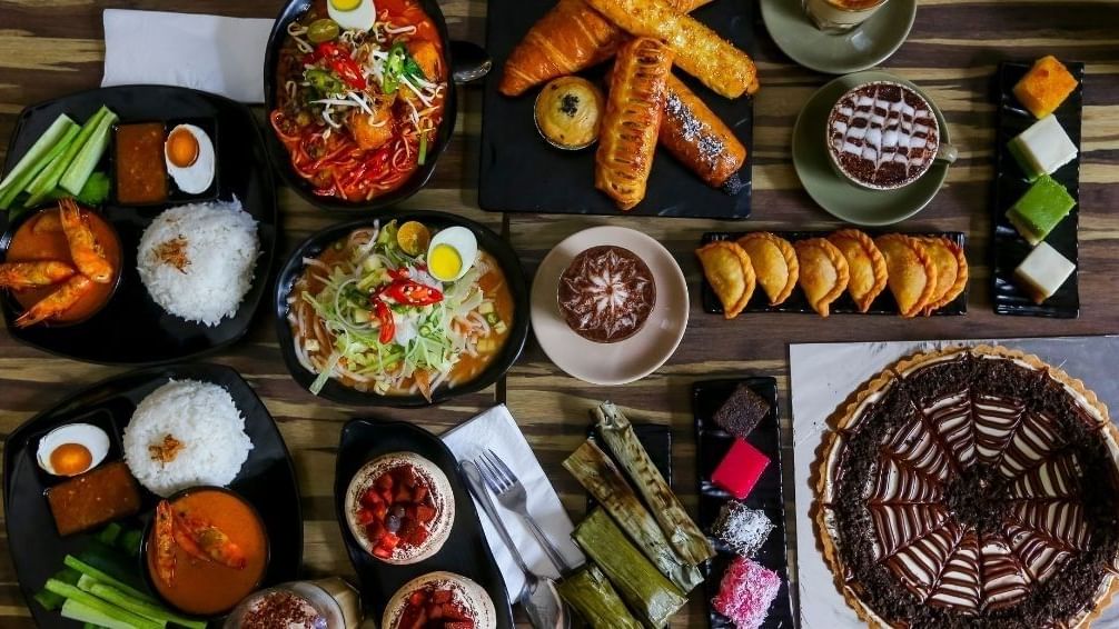 Various delicious dishes and desserts neatly arranged on black plates on a wooden table.