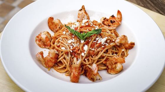 Pasta con camarones a la parrilla, queso desmenuzado y albahaca fresca en plato blanco en La Pérgola, Araiza Palmira 