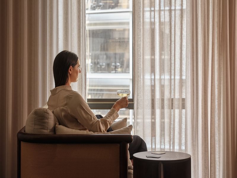 Woman relaxing in a hotel room with a glass of wine by the window.