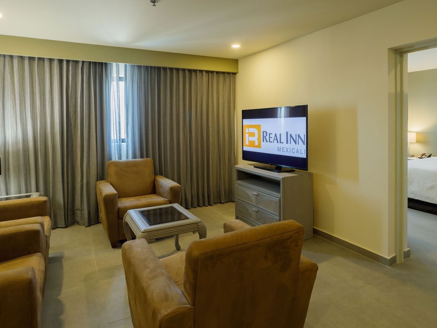 King Master Suite living area featuring plush tan armchairs and a large flat-screen TV at Real Inn Mexicali