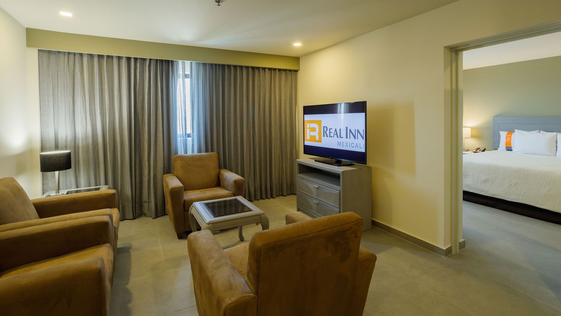 King Master Suite living area featuring plush tan armchairs and a large flat-screen TV at Real Inn Mexicali