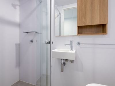Clean modern bathroom with shower stall, white sink, and wooden cabinet at UniLodge Brisbane City.