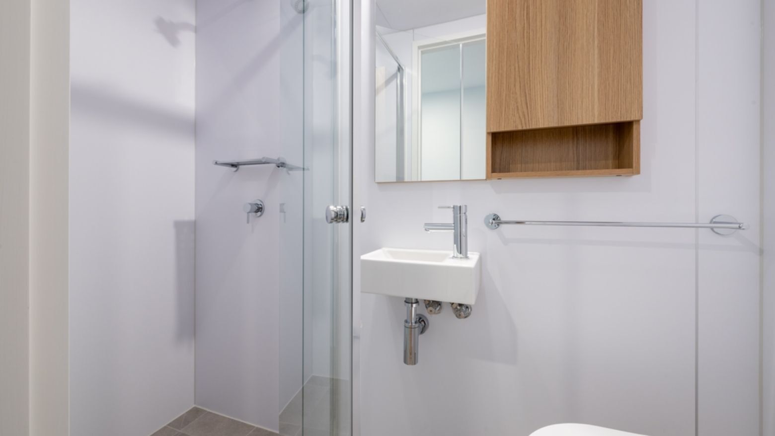 Clean modern bathroom with shower stall, white sink, and wooden cabinet at UniLodge Brisbane City.