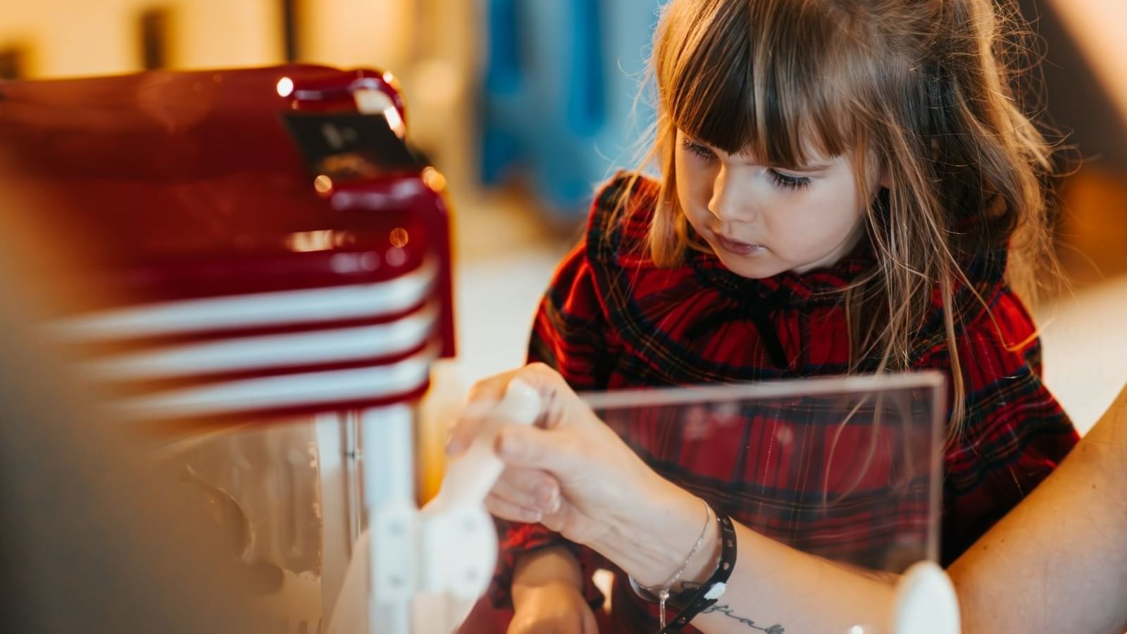 Close-up of a young girl in a red plaid dress receiving a treat from someone at Paramount Hotel Dubai