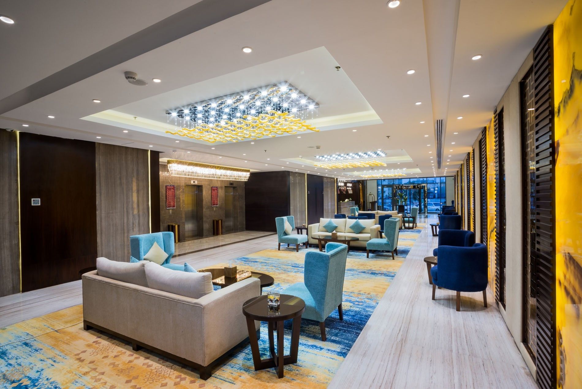 Blue chairs by small tables under bright ceiling lights in the lounge at Naviti By Warwick Dammam