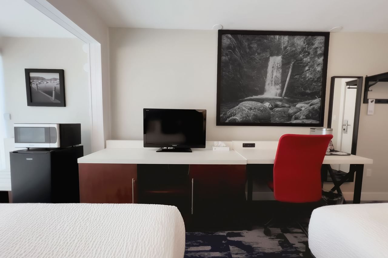 A guest room with king bed, tv, chair, desk, lamp, fridge, microwave