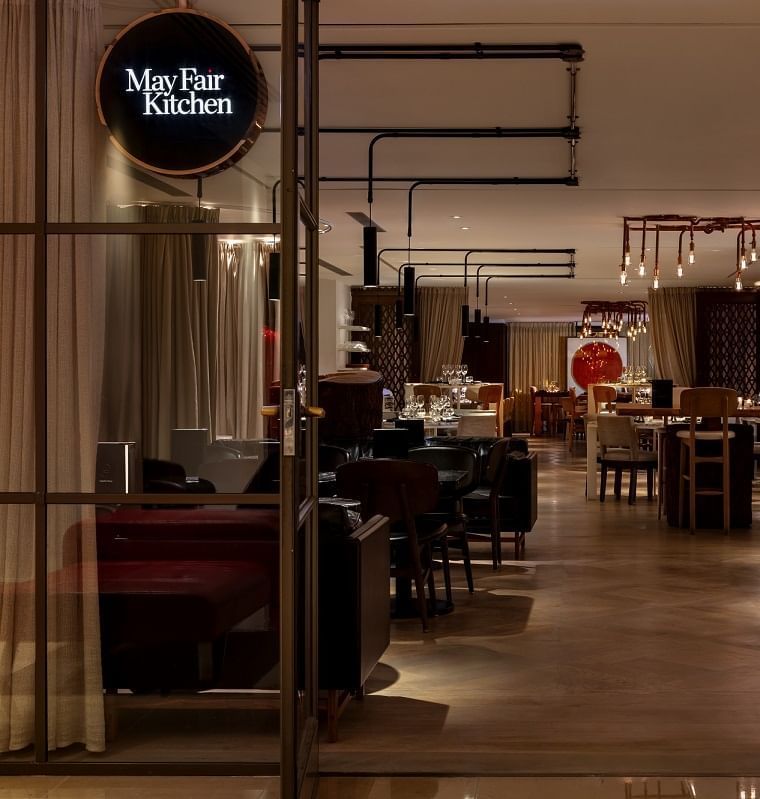 Entrance to a restaurant with a glass door, showcasing a modern dining area in May Fair Kitchen at The May Fair Hotel