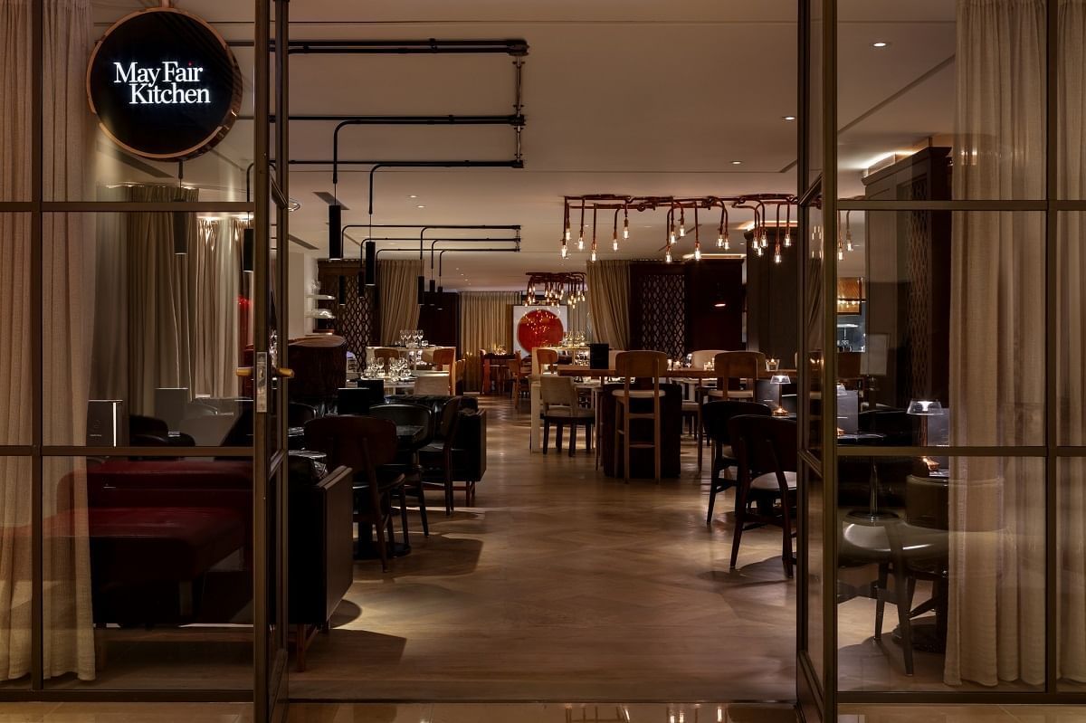 Entrance to a restaurant with a glass door, showcasing a modern dining area in May Fair Kitchen at The May Fair Hotel