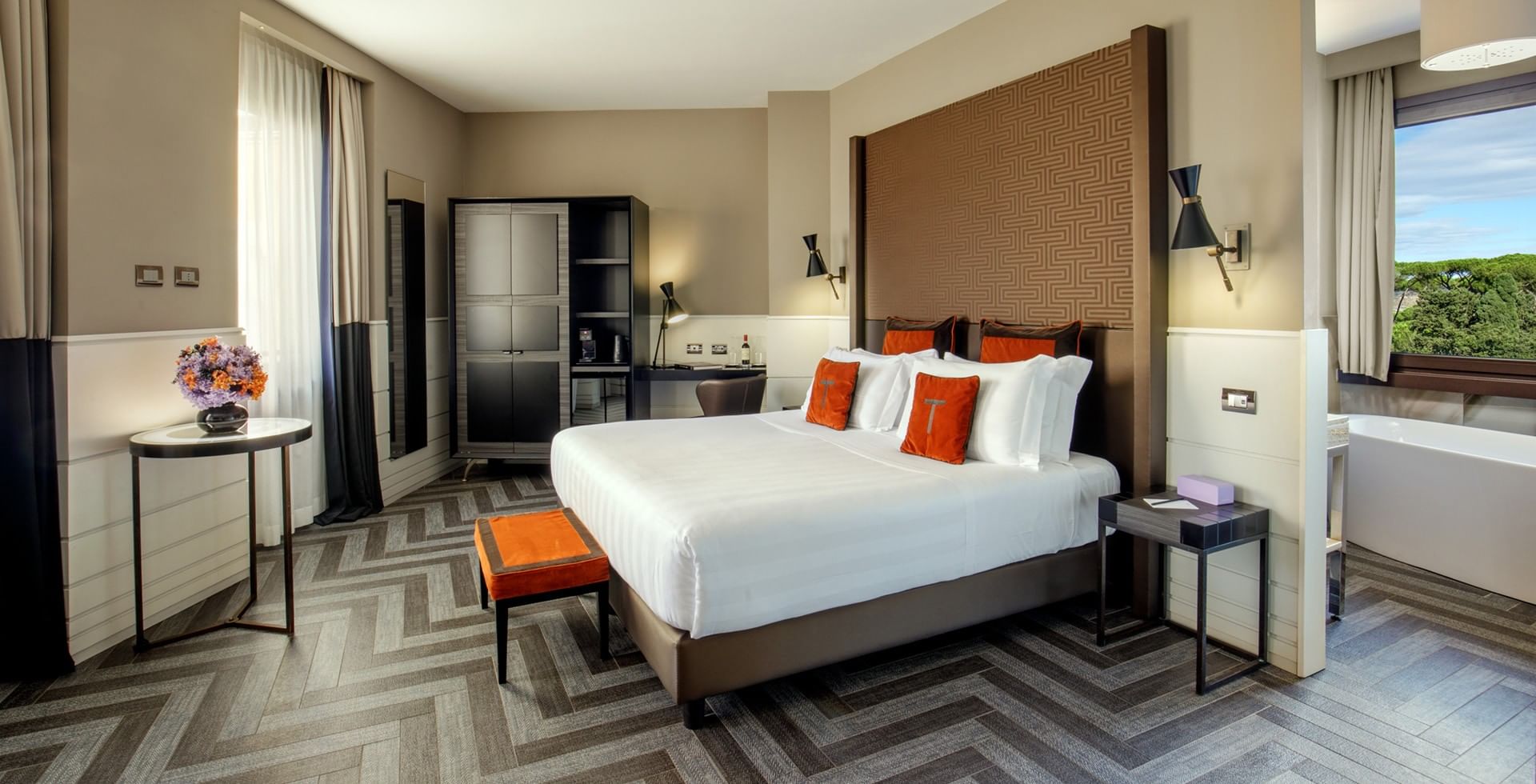 King Junior Suite Deluxe at Tribune Hotel Rome featuring a spacious king bed, modern décor with orange accents, elegant furnishings, and large windows with city and greenery views