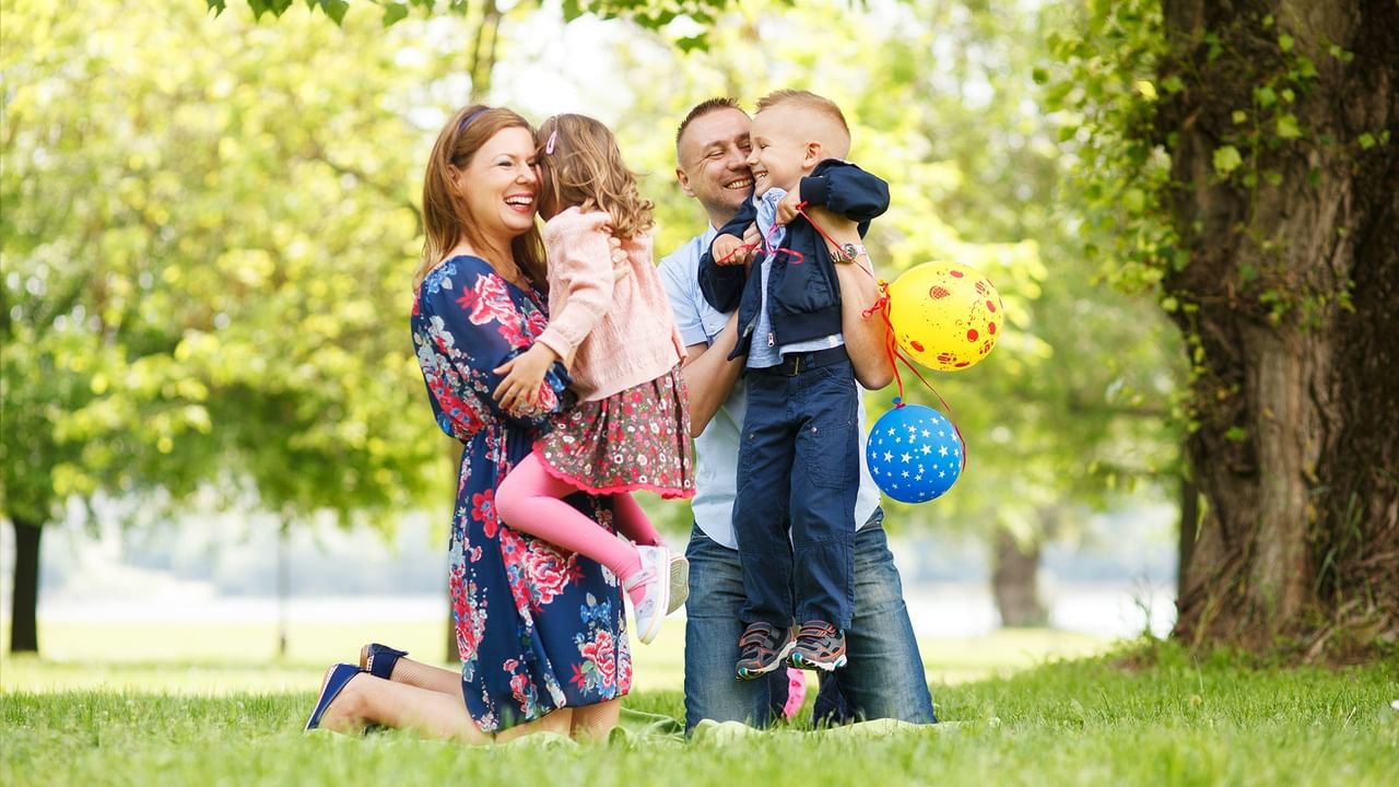 Family of four enjoying a sunny day outdoors in a park with colorful balloons for Summer Savings.