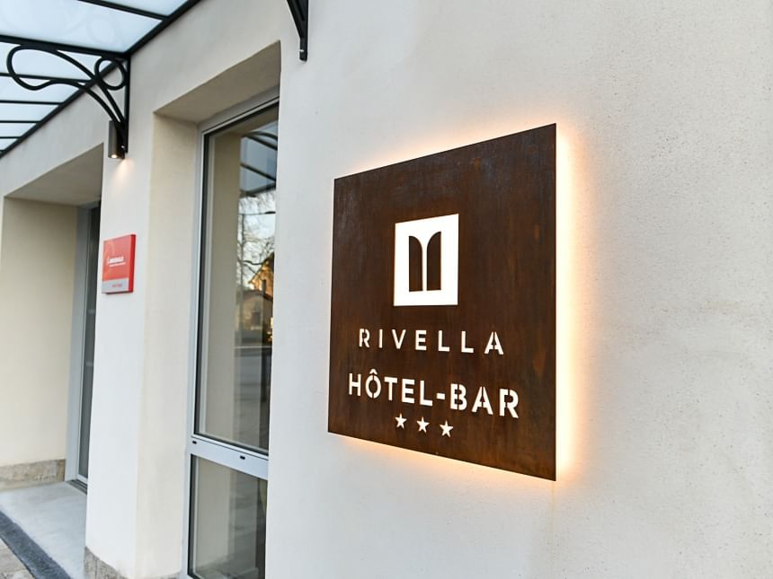 Enseigne lumineuse hôtel-bar Rivella sur mur de bâtiment beige