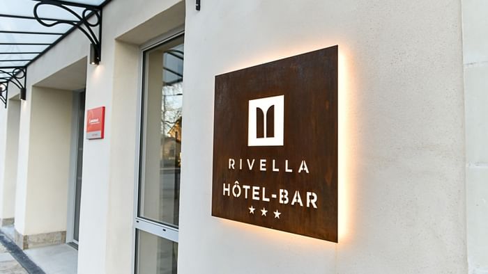Enseigne lumineuse hôtel-bar Rivella sur mur de bâtiment beige