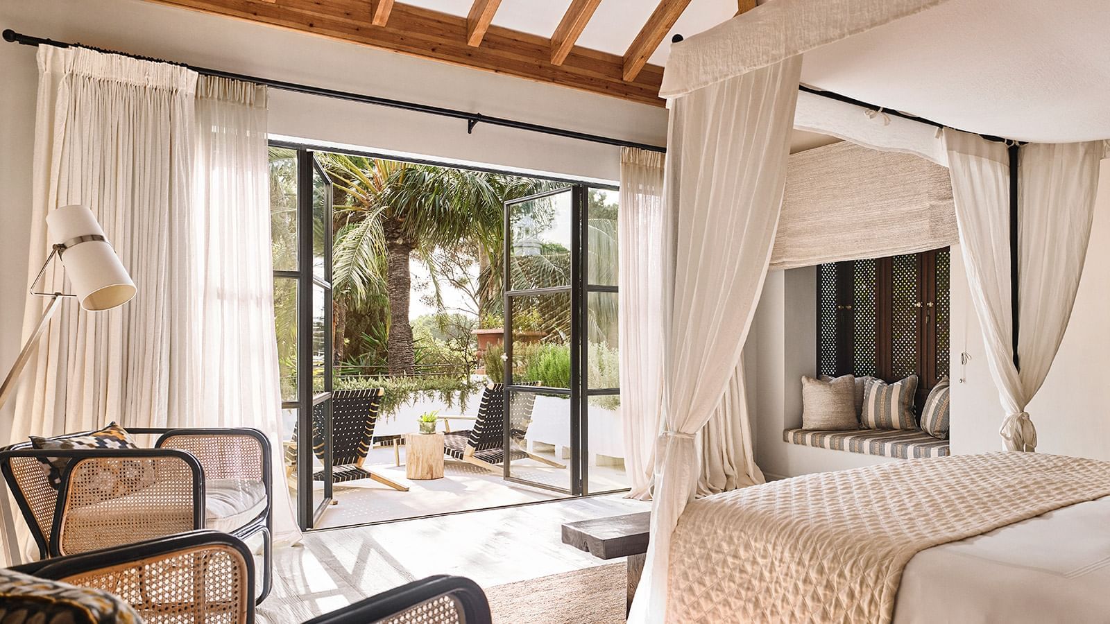 Bedroom with a canopy bed near glass doors that open to a terrace with wicker chairs at the Marbella Club
