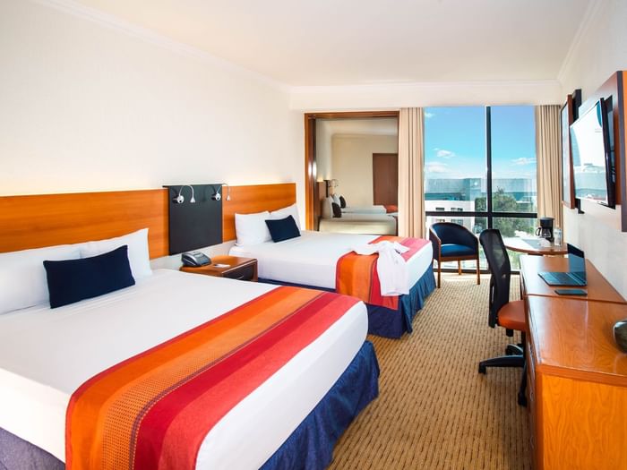 Suite with two beds featuring a desk & an ocean view in the distance, at the Guadalajara Plaza Hoteles & Suites