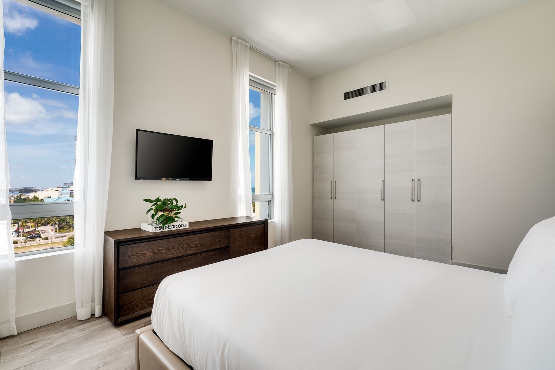 A clean and modern guest room with a large bed, wooden dresser, flat-screen TV, and closet.