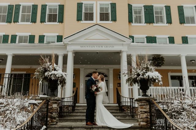 Bride and groom standing close on a white footbridge, near mountains and pines at Mountain View Grand Resort & Spa