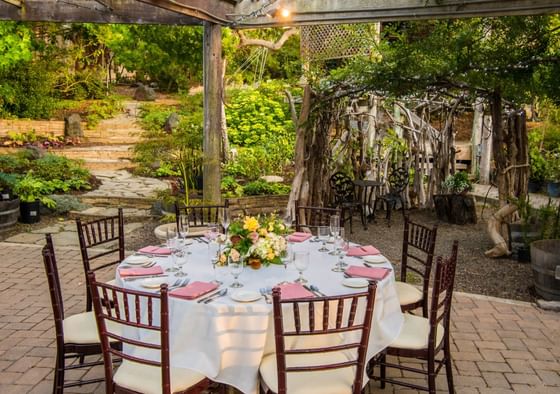 Outdoor garden dining table set with white linens and pink napkins under a pergola at Cambria Pines Lodge