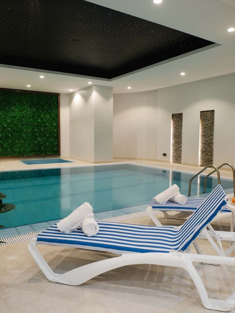 Striped lounge chairs with towels by an indoor pool under a black ceiling at Cantonal Hotel by Warwick Riyadh