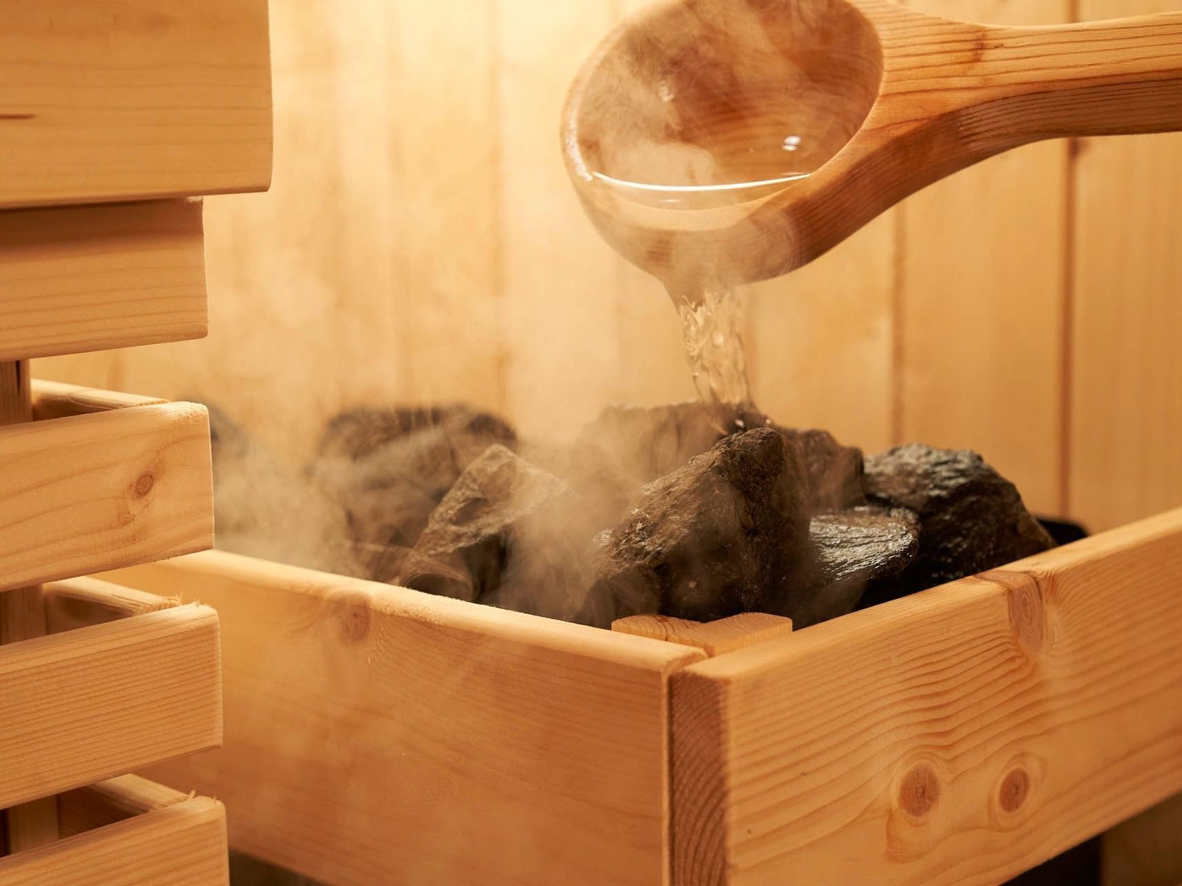 A wooden ladle pours hot water over sauna stones, releasing steam in the warm masonry setting at Orchard Grand Court