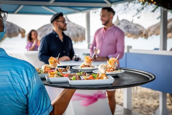 Waiter serving appetizers to guests by the shore at Passions on the Beach