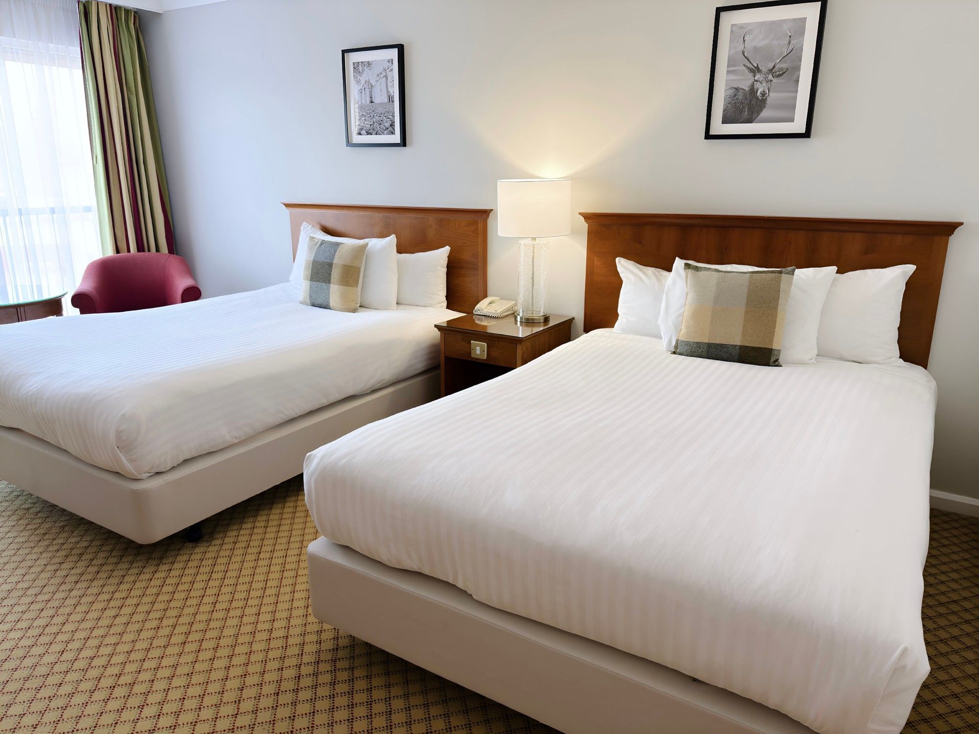 Spacious family room at Aberdeen Dyce Hotel featuring two double beds, crisp white linens, and a cosy red armchair.