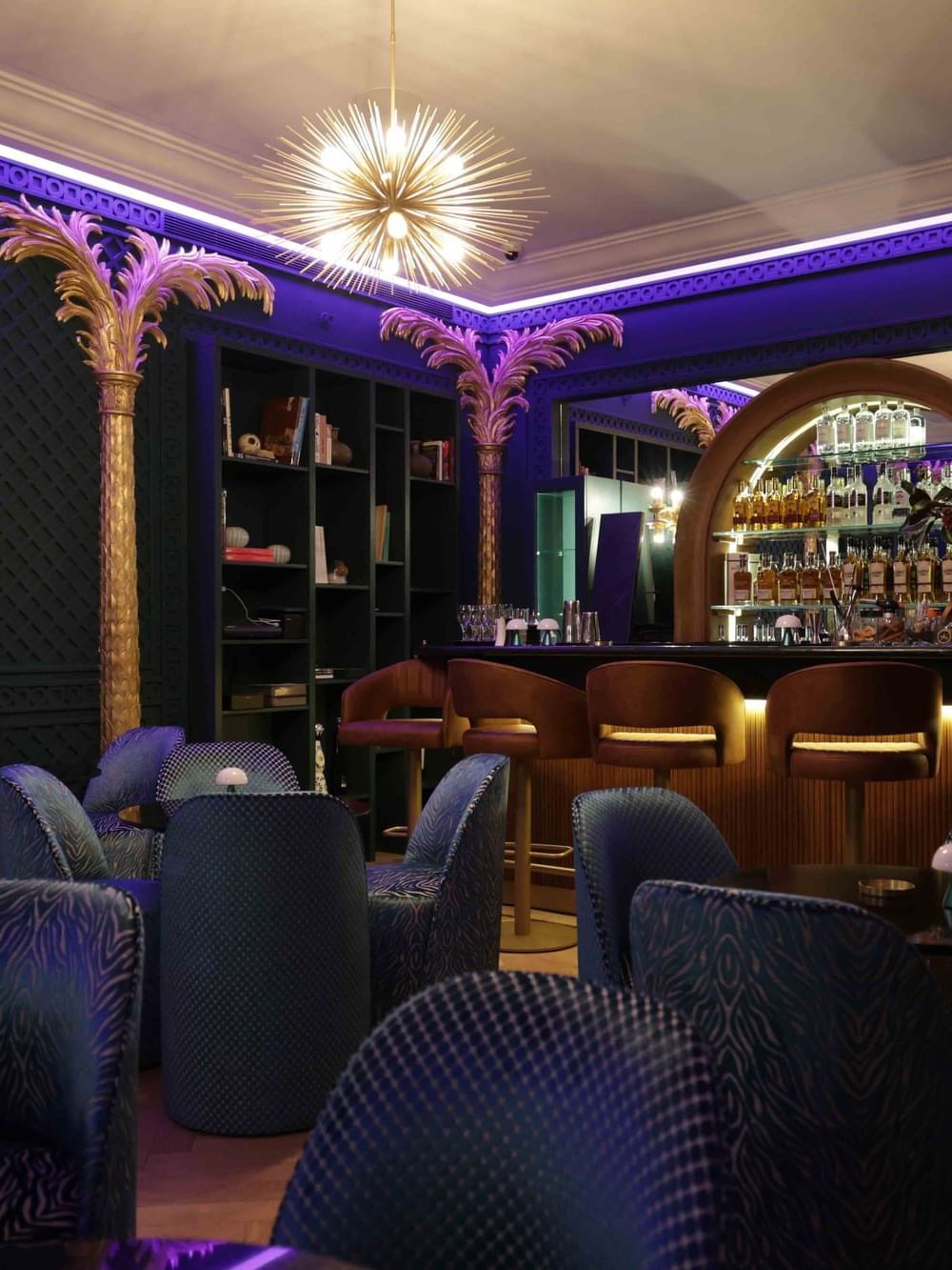 Blue seating by the bar counter with liquor shelves at The Bar in Warwick Palm Beach Hotel