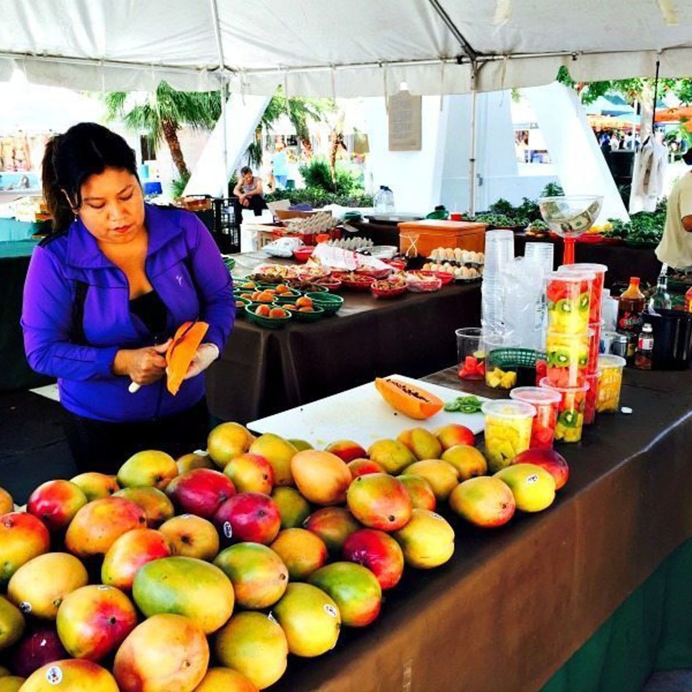Outdoor fruit vendor preparing fresh papaya slices behind a table piled high with mangoes near Tradewinds Apartment Hotel