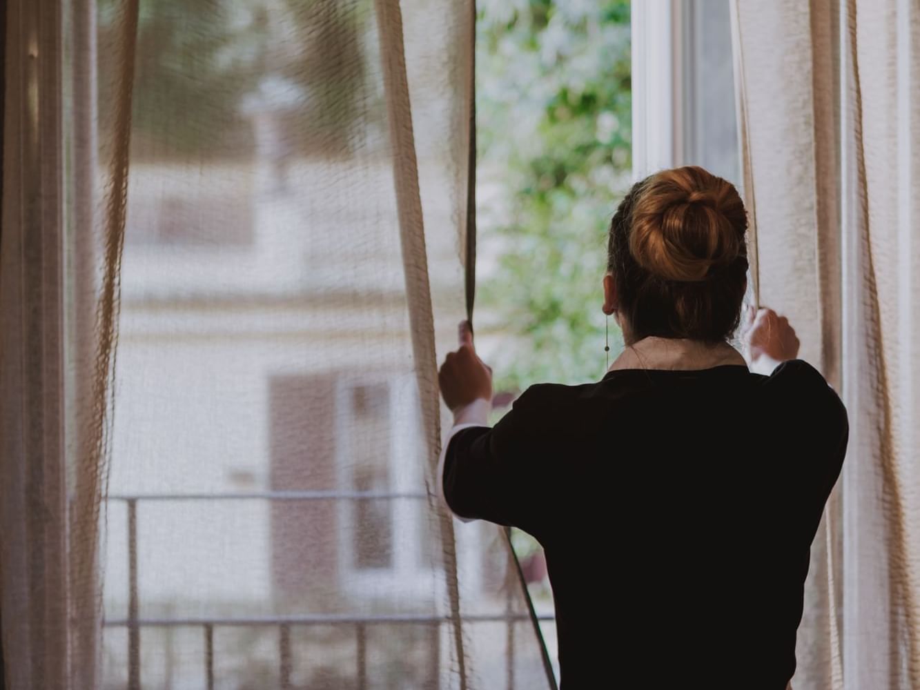 A woman looking out a window through sheer curtains at Margutta 19
