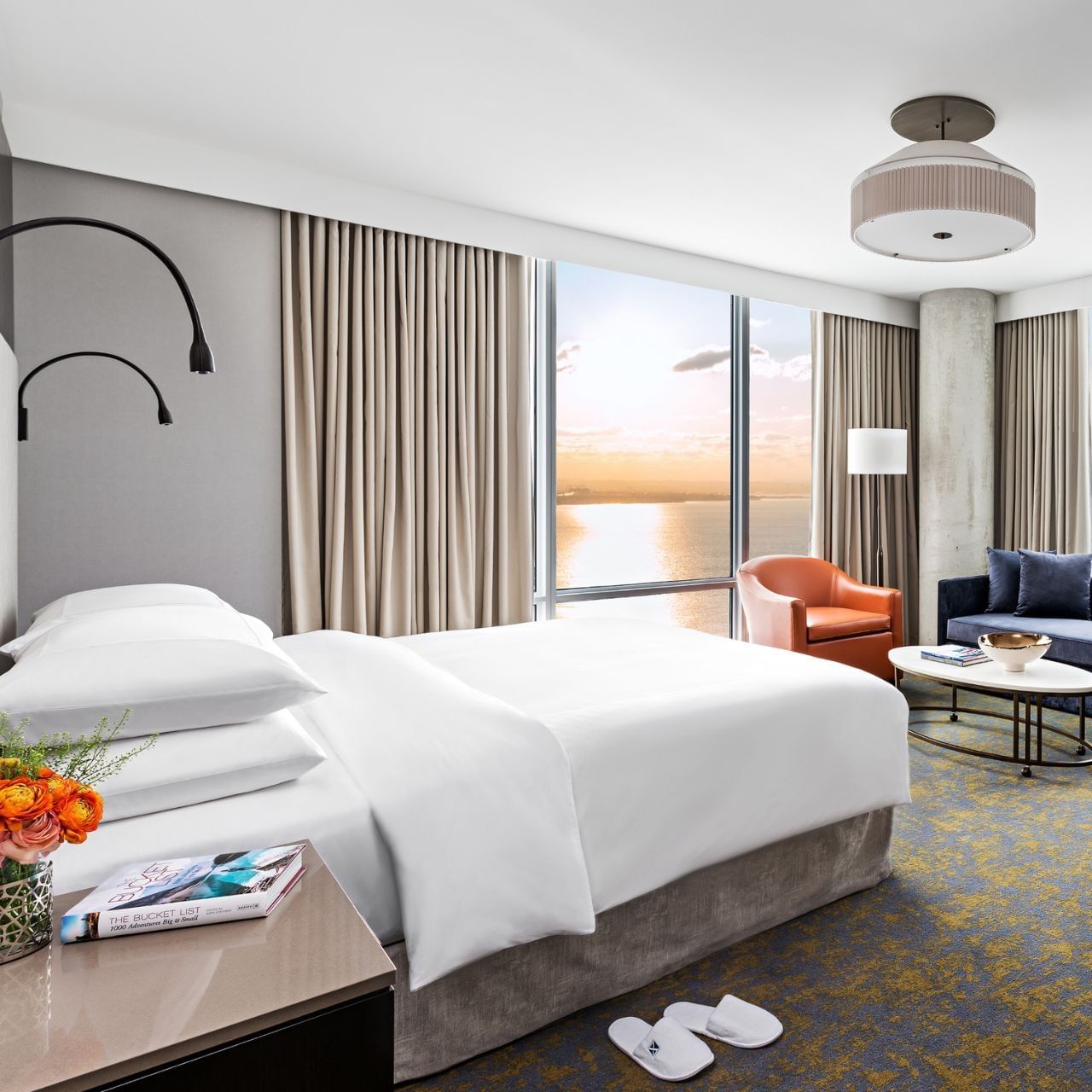 Guest room at Hotel X Toronto, with a white bed by floor-to-ceiling windows overlooking the ocean, and an orange chair