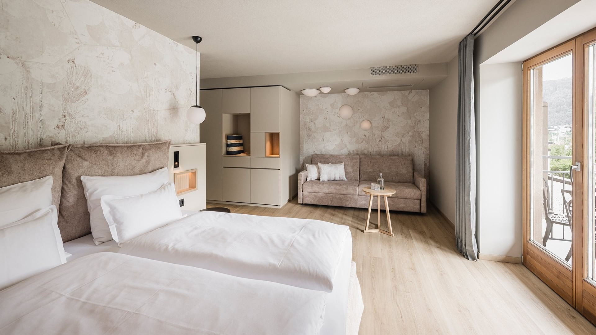 Camera da letto con due letti, divano, tavolo e portefinestre che conducono al balcone.
