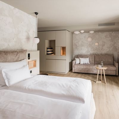 A modern hotel room with two beds, a couch, and a balcony with a view.