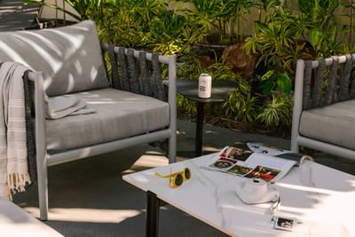 Patio seating with gray chairs, a marble table, a magazine, and sunglasses at Kenmore Village Hotel, South Beach Miami hotels
