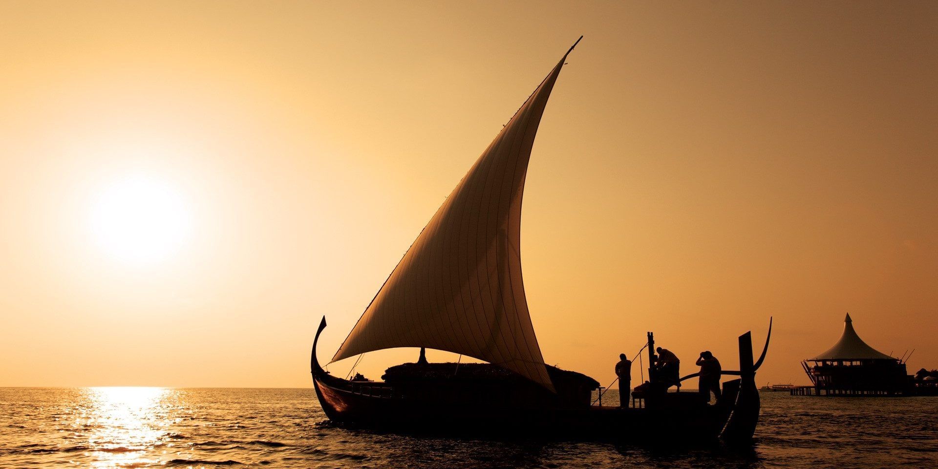 Silhouetted sailboat with people at sunset on the sea near Grand Park Kodhipparu, Maldives