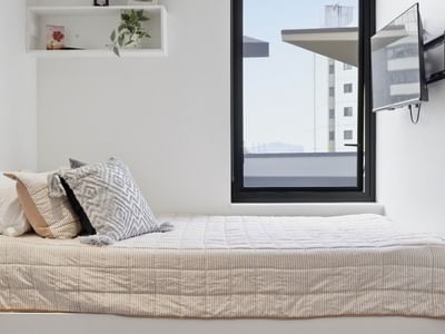 Cozy room with white walls, bed, TV, and view of a tall building at UniLodge Auckland City.