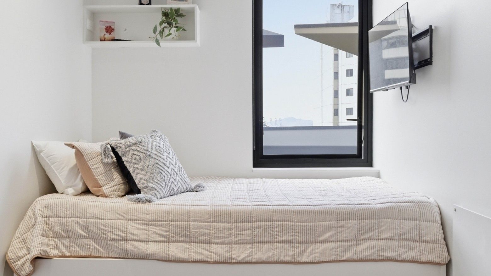 Cozy room with white walls, bed, TV, and view of a tall building at UniLodge Auckland City.