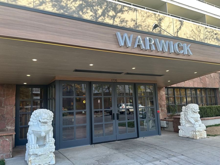 White stone lions guard the Warwick Denver entrance near the wooden awning and glass doors