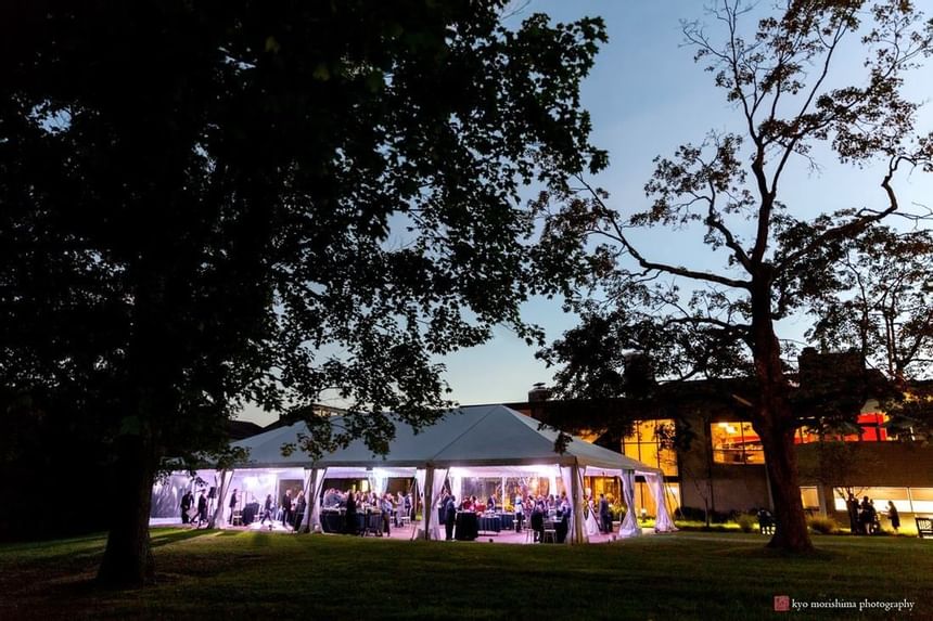 Evening outdoor wedding reception under illuminated white tent beside conference center at Aramark Chauncey Conference Center