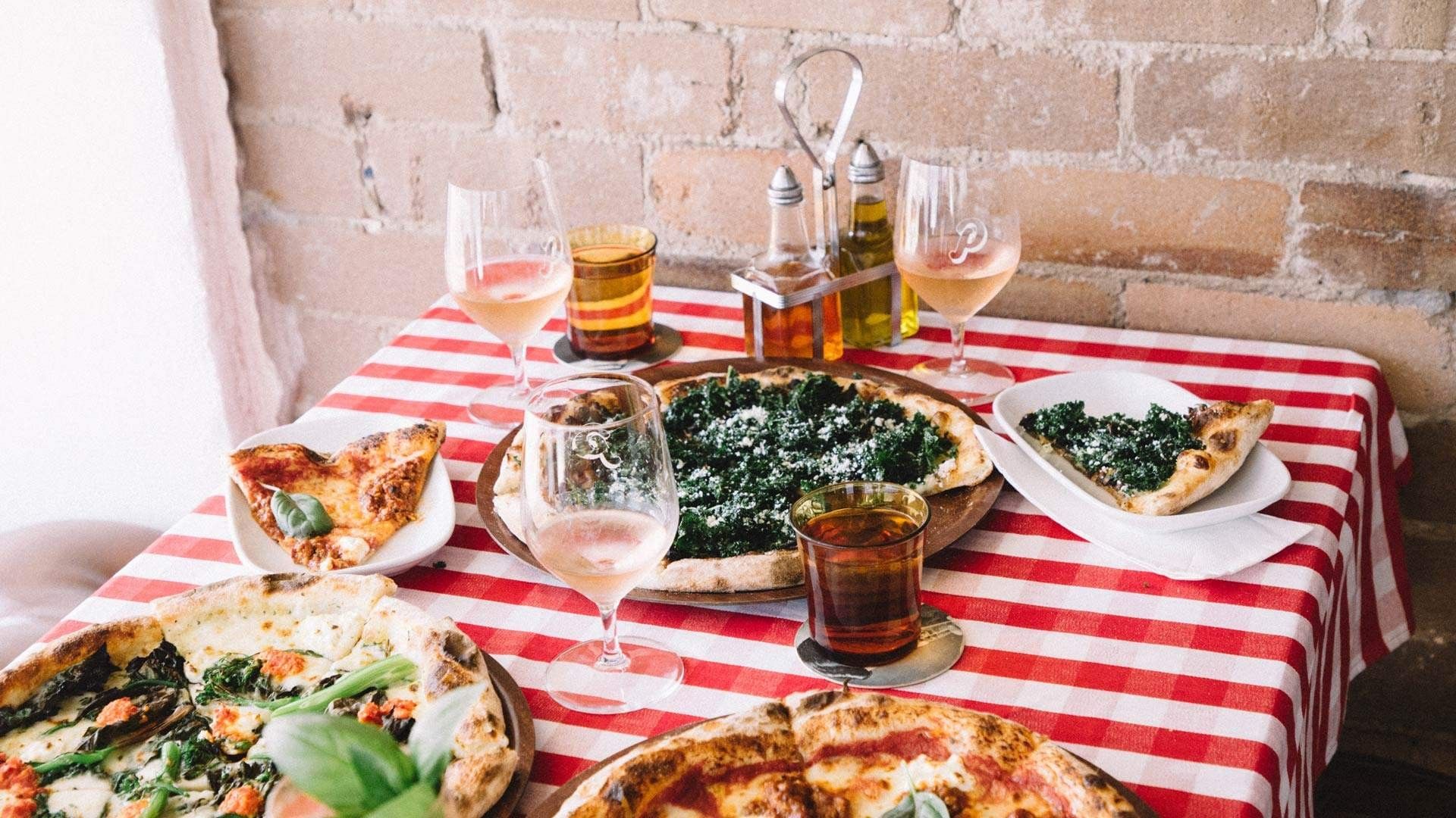Pocket Pizza at Elysium Hotels is a cozy restaurant on a red checkered tablecloth with various pizzas and rosé wine