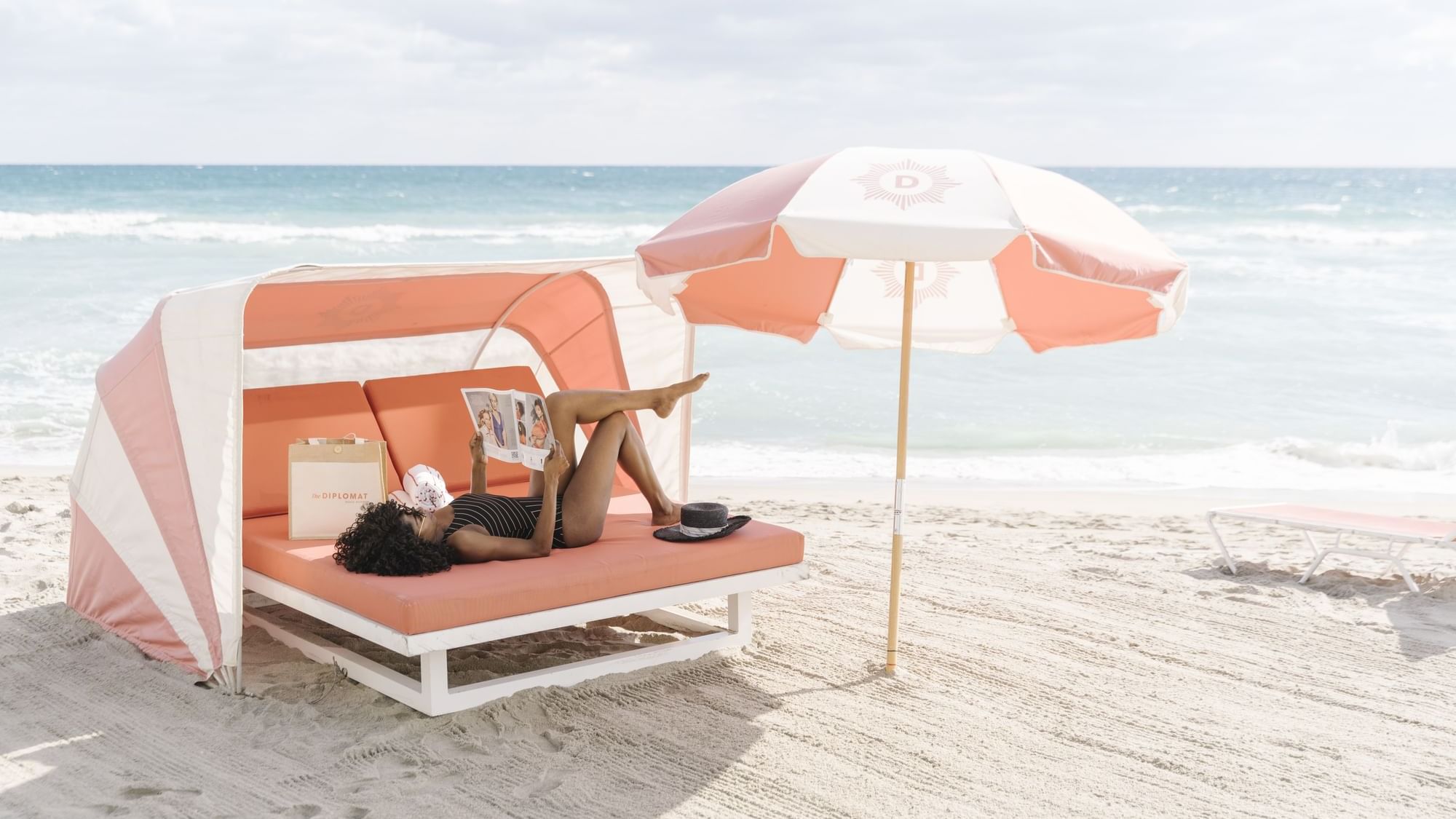 A woman relaxing on a beach chair under an umbrella at The Diplomat Resort