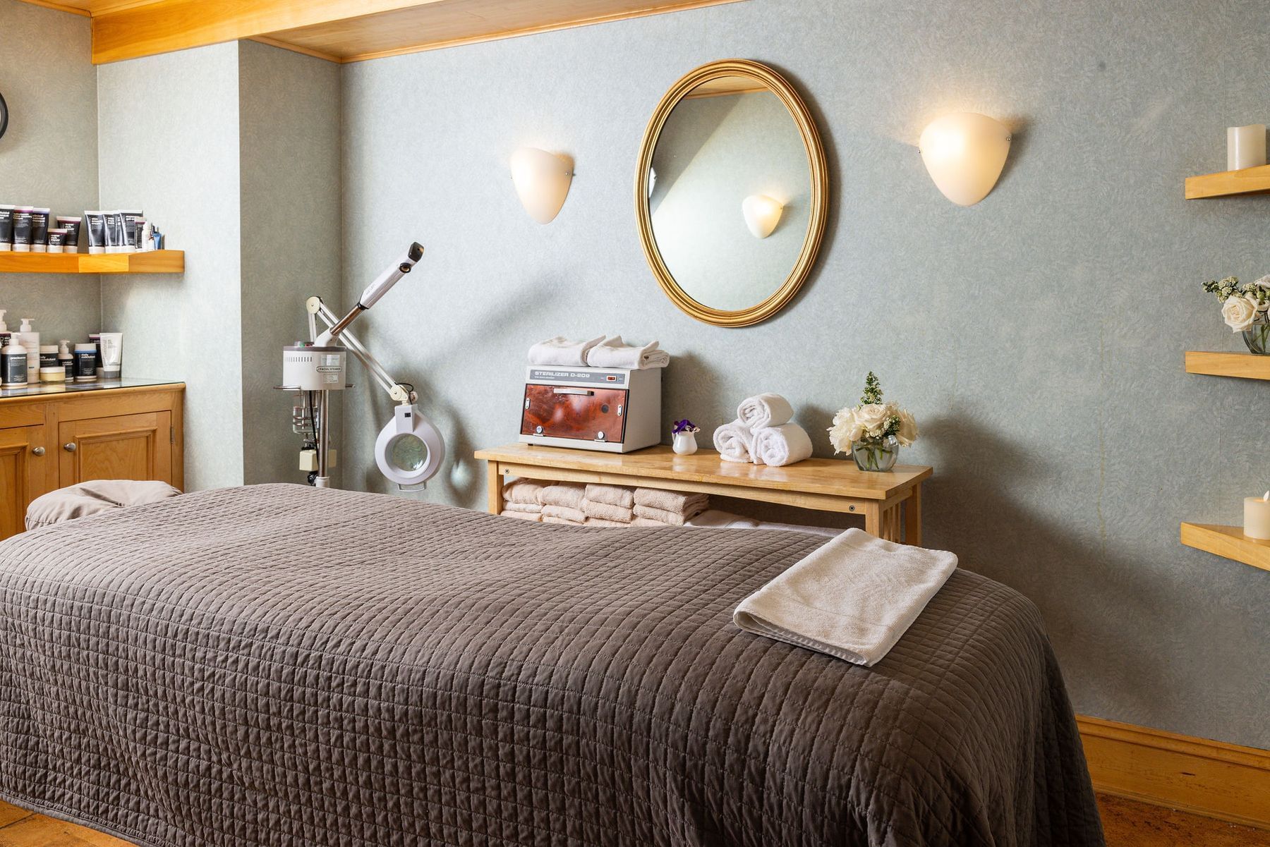 Massage room at the Regency Hotel and Spa with a bed, mirror, towels, towels, flowers, and a wall-mounted lamp.