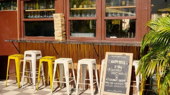 Outdoor bar with colorful yellow and white stools and happy hour chalkboard sign at Clinton Hotel and Spa